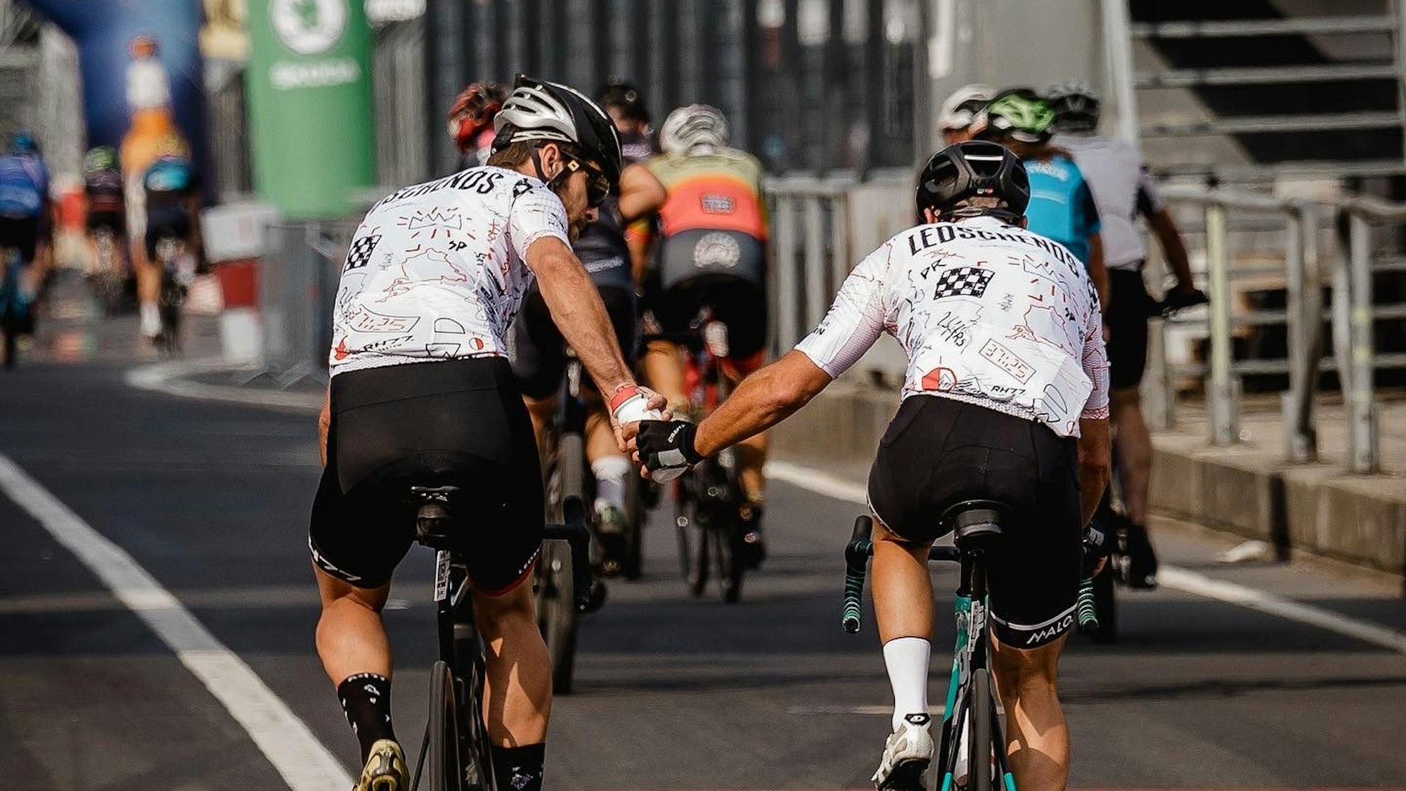 Zwei Radfahrer des Teams Ledschends überreichen sich während der Fahrt eine Trinksflasche.