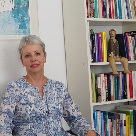 Eine Frau sitzt neben einem Bücherregal.