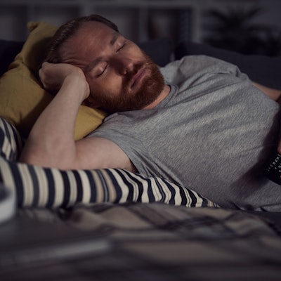 Bild eines bärtigen erwachsenen Mannes, der auf dem Sofa beim Fernsehen eingeschlafen ist.