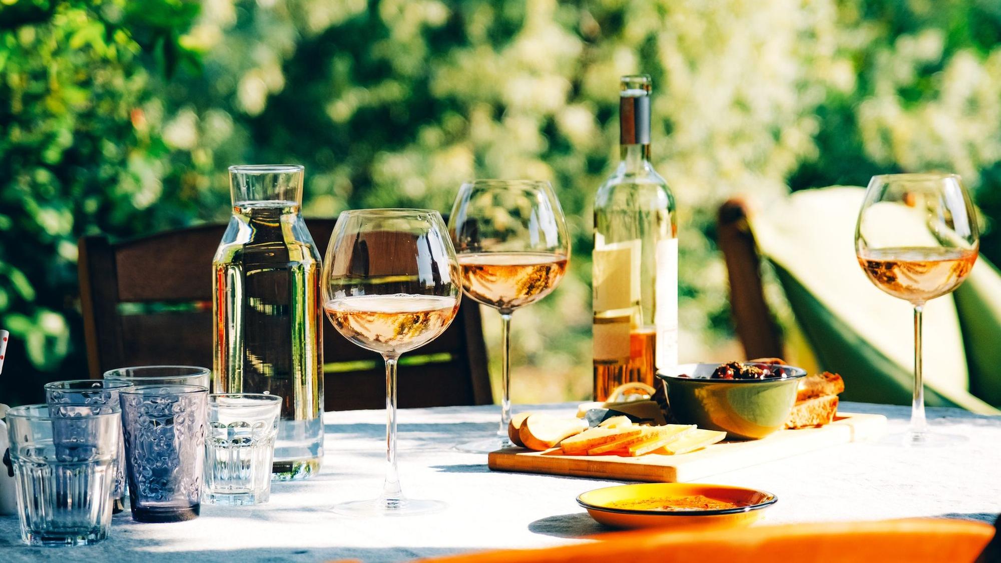 Roséwein im Glas und in der Flasche auf einem sommerlich gedeckten Tisch im Grünen