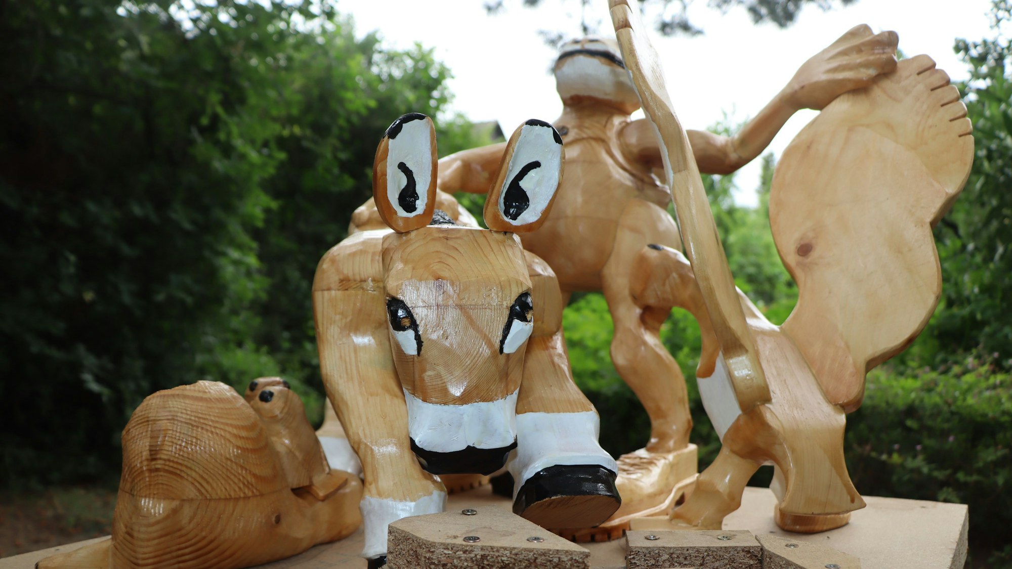 Zu sehen ist eine hölzerne Skulptur. Sie zeigt einen Esel, eine Ente und eine Kröte.