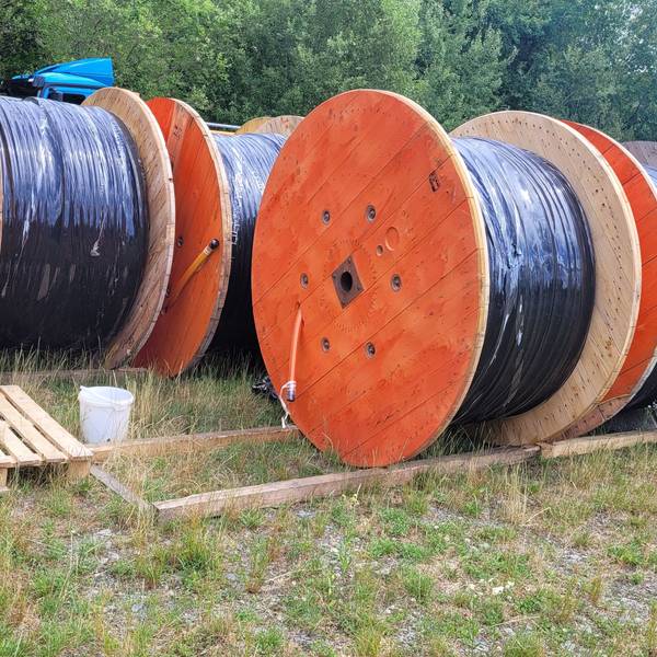 Glasfaserkabel auf großen Kabeltrommeln warten am Rande einer Baustelle auf den Einbau.