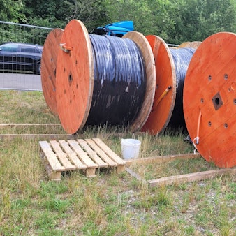 Glasfaserkabel auf großen Kabeltrommeln warten am Rande einer Baustelle auf den Einbau.