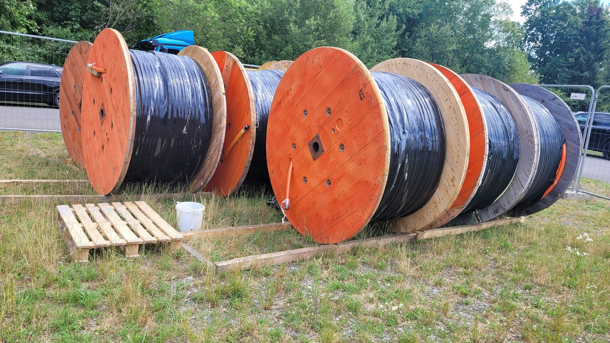 Man sieht riesige Kabeltrommeln auf einer Wiese liegen.