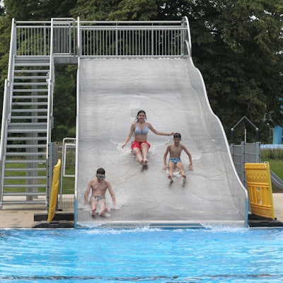 Drei Kinder rutschen eine Wasserrutsche in einem Schwimmbad herunter.