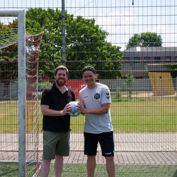 Zwei Männer stehen vor einem Fußballtor und halten einen Fußball in den Händen.