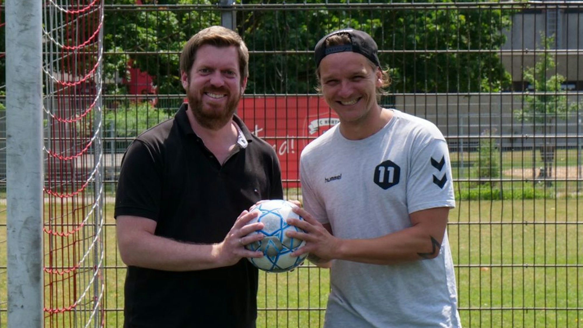Zwei Männer stehen vor einem Fußballtor und halten einen Fußball in den Händen.