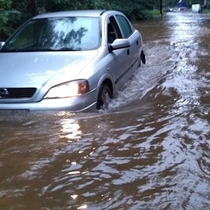Ein Auto steckt im Hochwassers in Dünnwald fest. Die gesamte Straße ist voller Wasser, es steht dem Auto bis zu den Lichtern.