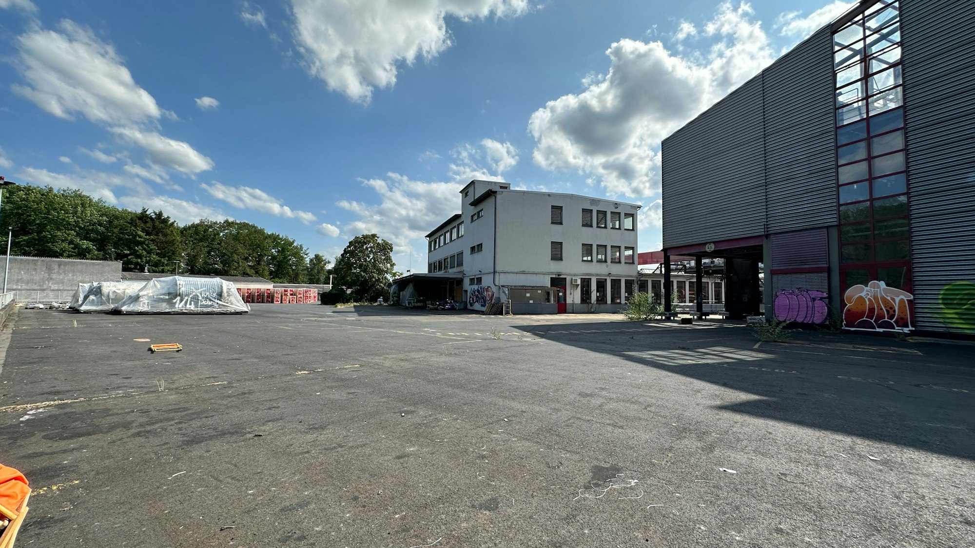 An einem riesigen freien Betonplatz stehen zwei große Farbikgebäude.