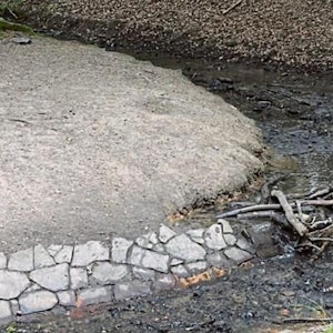Wasserentnahme mit einem Kanister aus einem Bach (nachgestellte Szene)