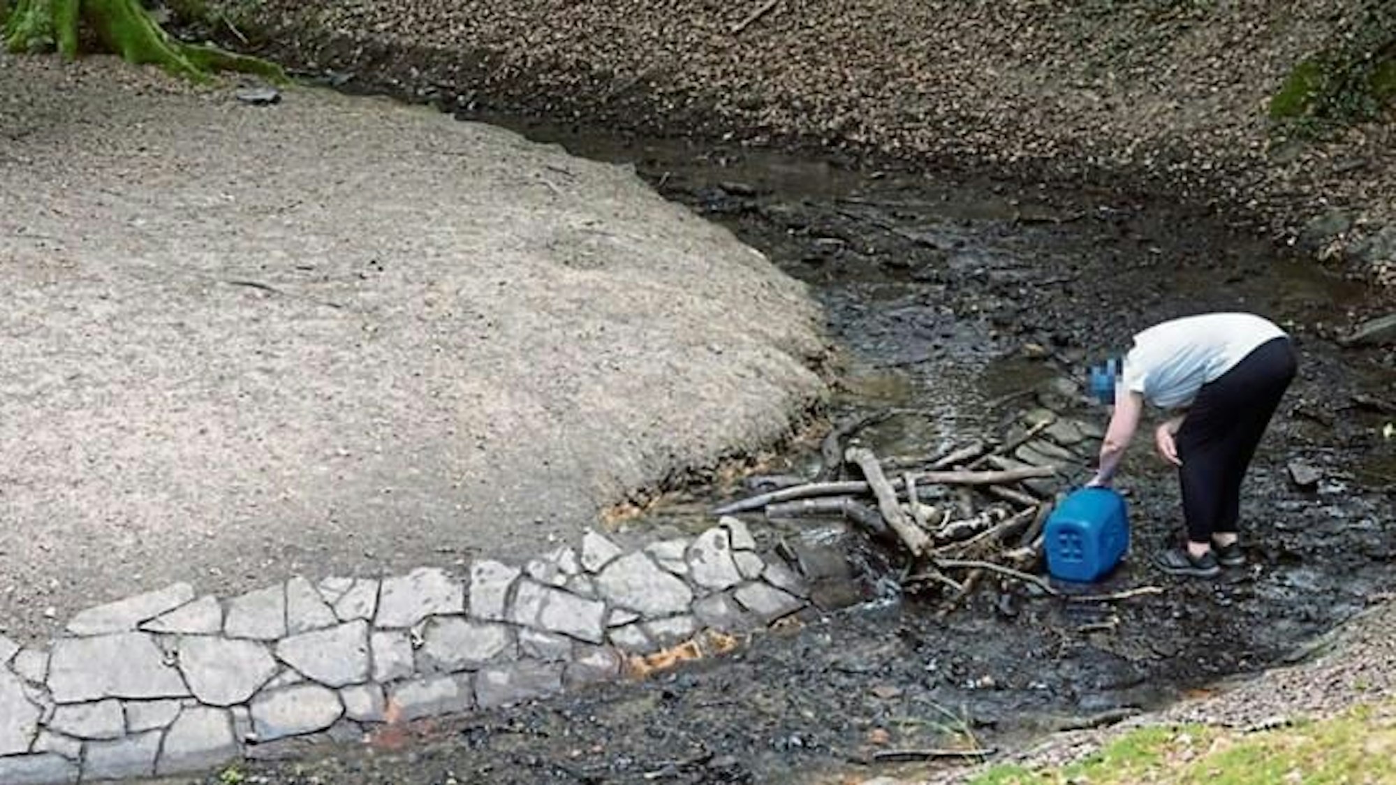 Wasserentnahme mit einem Kanister aus einem Bach (nachgestellte Szene)