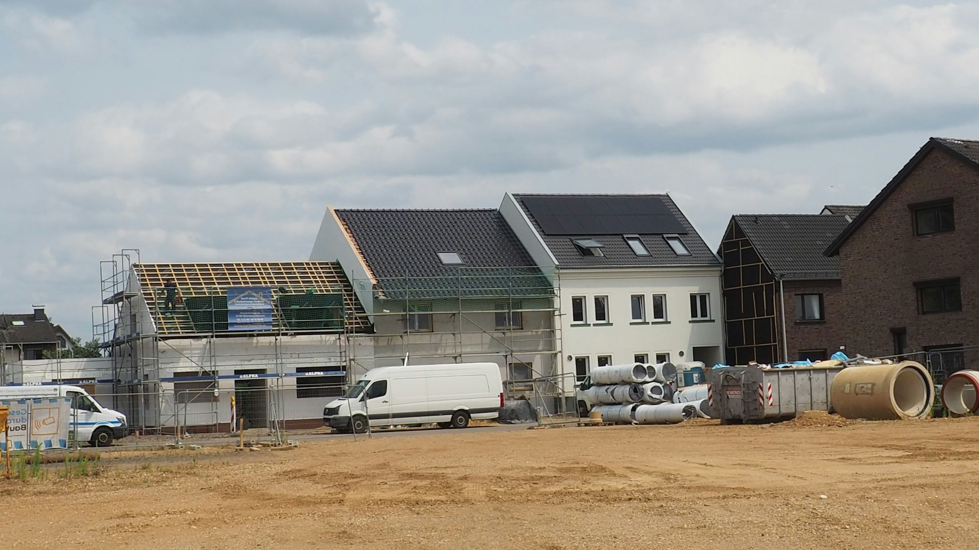 Hinter einer Sandfläche stehen drei Häuser, an zweien sind noch Baugerüste zu sehen.