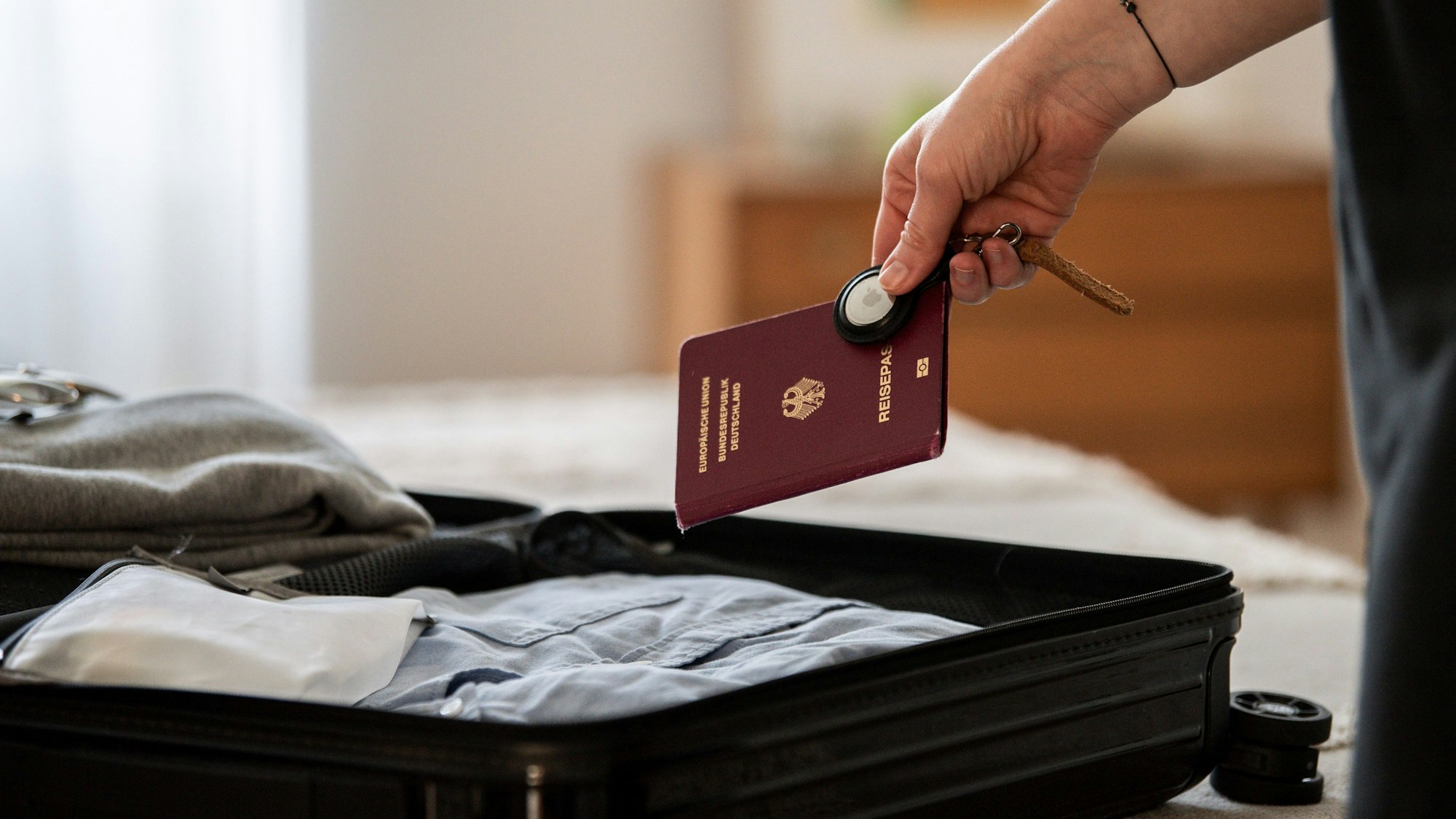 Ein Reisepass wird gemeinsam mit einem Koffer-Tracker in einen Koffer gelegt.