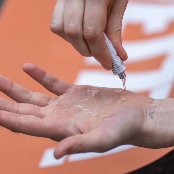 Eine Klimaaktivistin der „Letzten Generation“ schmiert sich Kleber auf die Hand. Im Hintergrund ist ein orangefarbenes Protest-Plakat zu sehen. (Symbolbild)