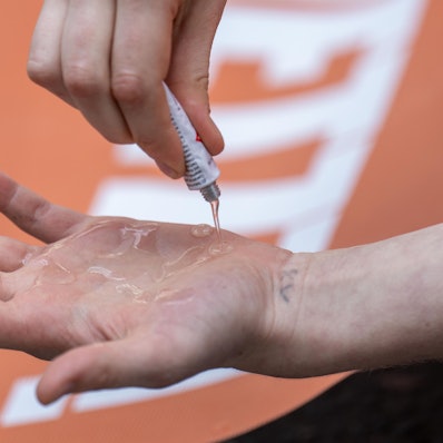 Eine Klimaaktivistin der „Letzten Generation“ schmiert sich Kleber auf die Hand. Im Hintergrund ist ein orangefarbenes Protest-Plakat zu sehen. (Symbolbild)