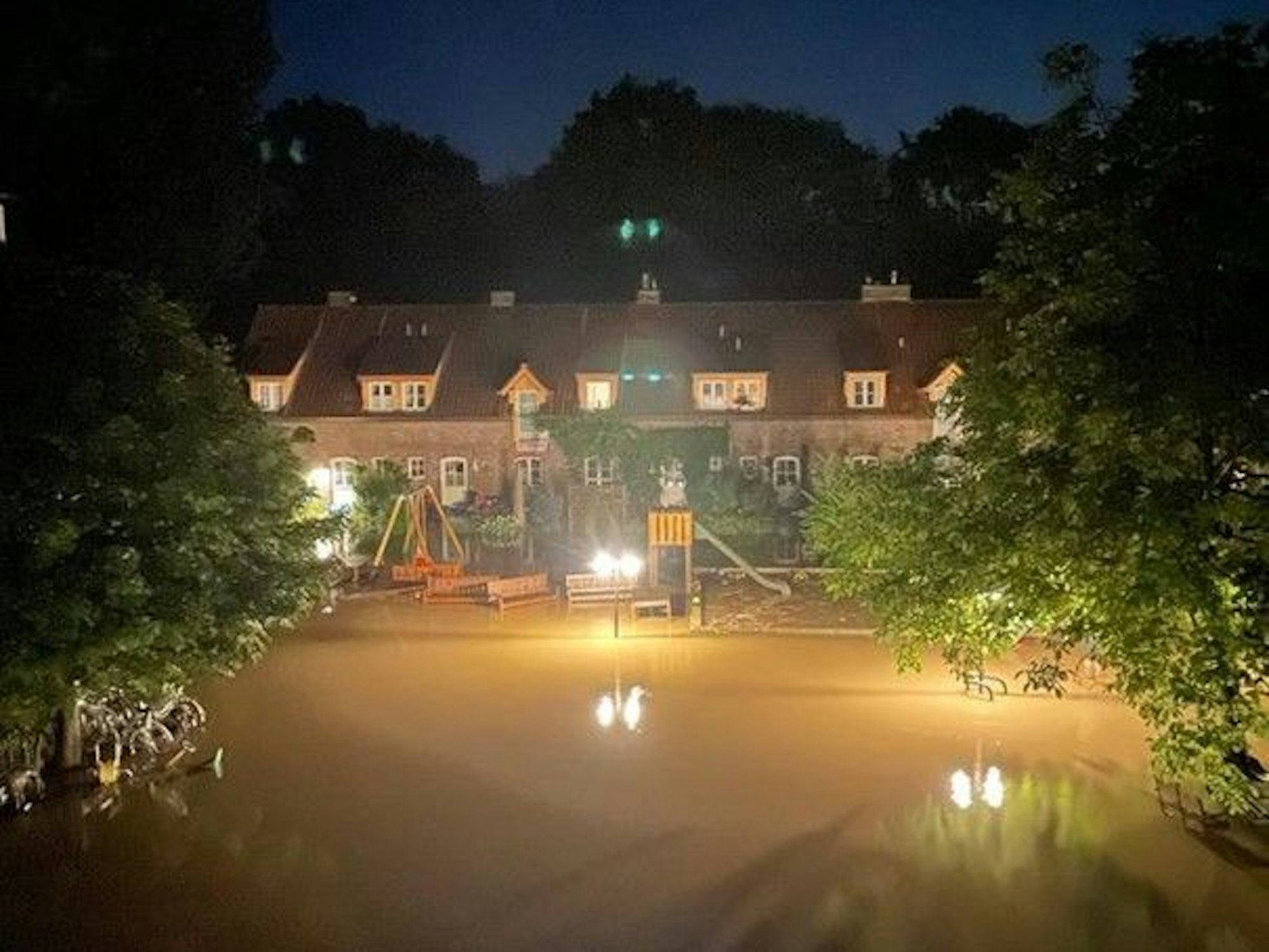 Eine Luftaufnahme bei Nacht von dem Hochwasser in Dünnwald. Ein Scheinwerfer beleuchet die Wassermassen, die die gesamte Straße bedecken.