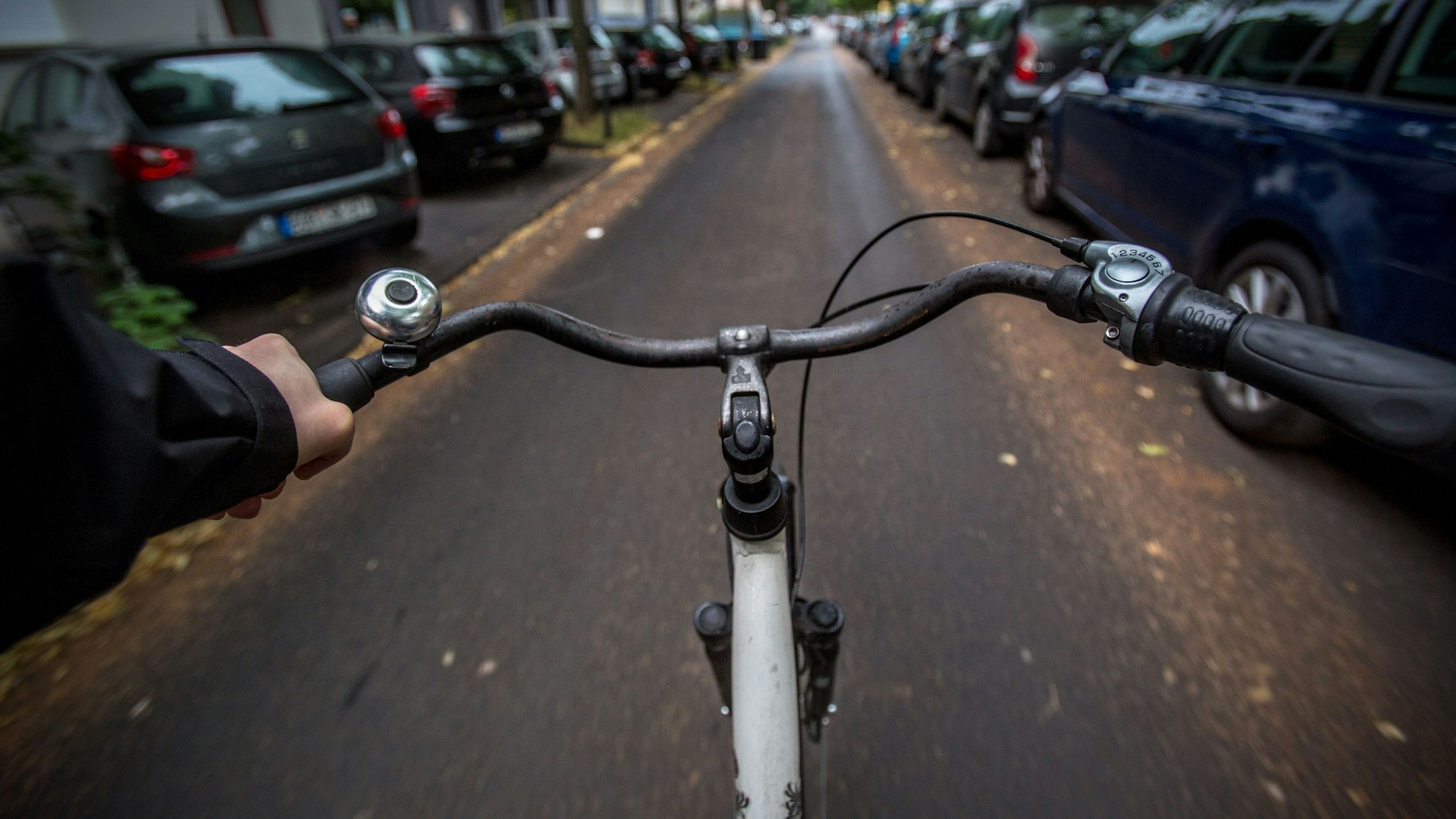 Aus der Perspektive eines Fahrradfahrers ist eine kleine Nebenstraße mit zahlreichen geparkten Autos zu sehen.