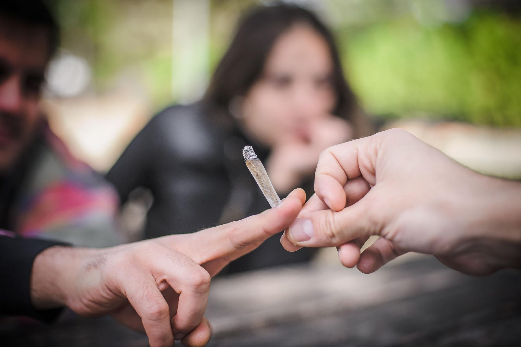 Nahaufnahme eines Joints, der von einer Hand zur nächsten gereicht wird.