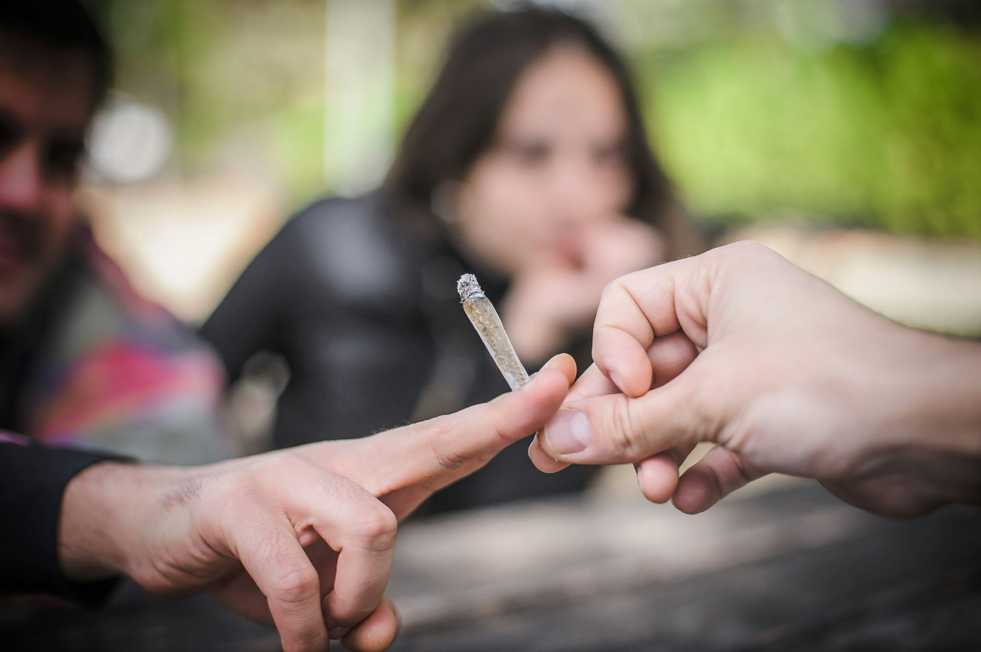 Nahaufnahme eines Joints, der von einer Hand zur nächsten gereicht wird.