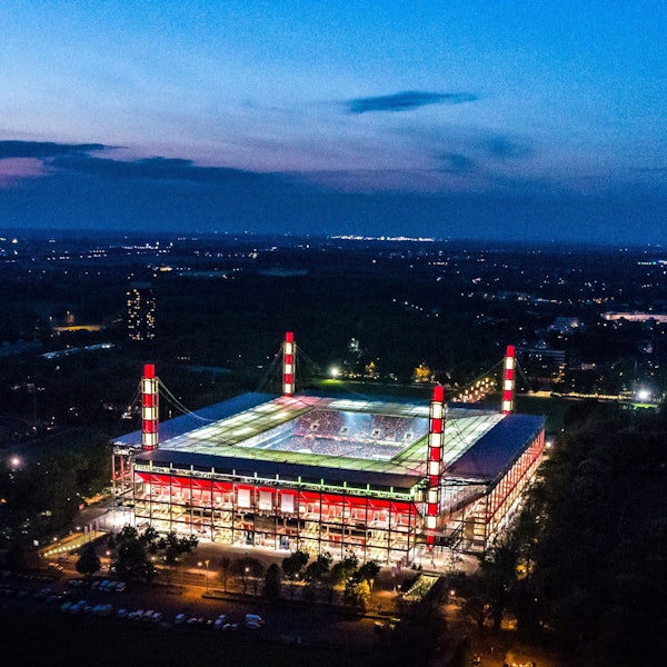 Außenansicht eines Fußballstadions während der Abenddämmerung, beleuchtet in den Farben Rot-Weiss