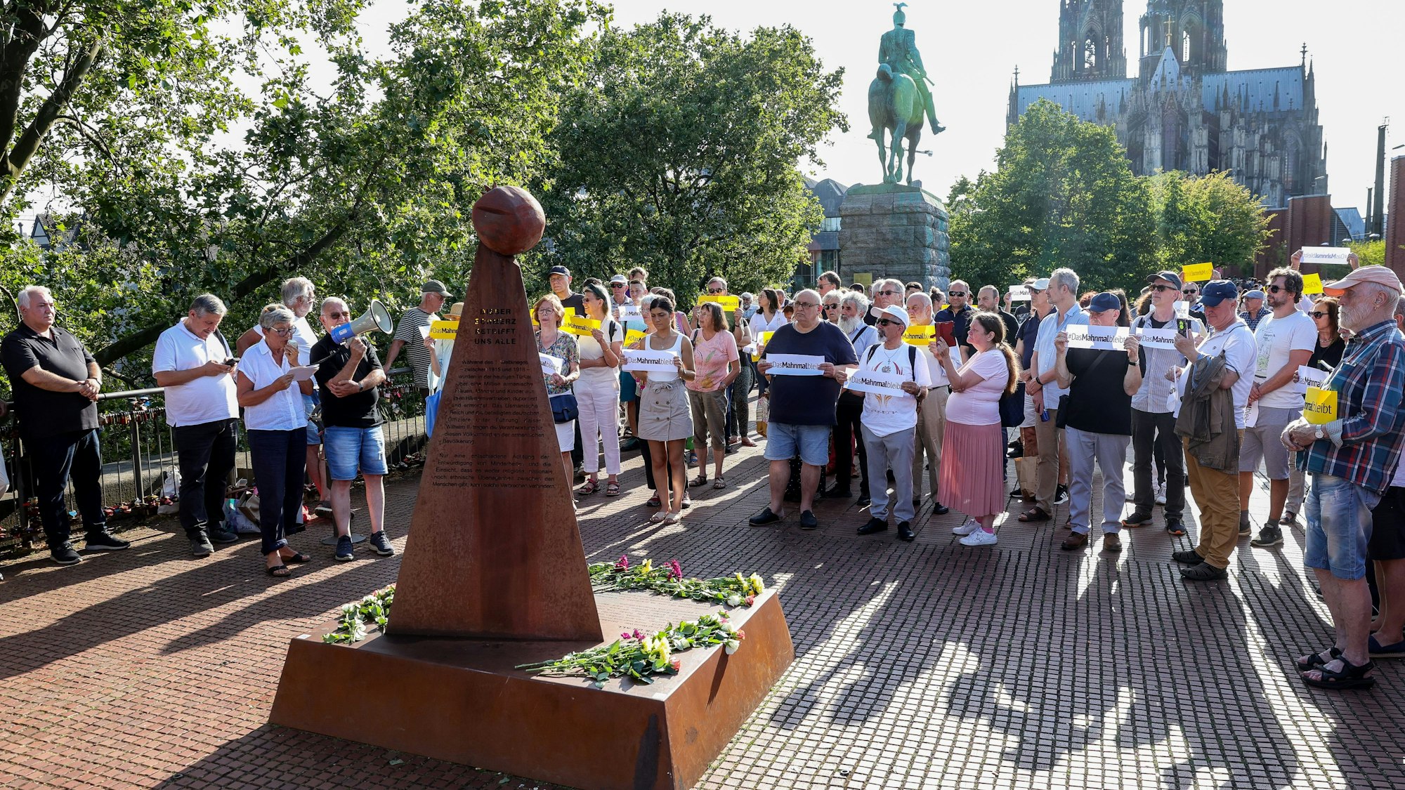 Eine Gruppe an Menschen versammelt sich um das Mahnmal zum Gedenken an den Völkermord an der armenischen Bevölkerung.