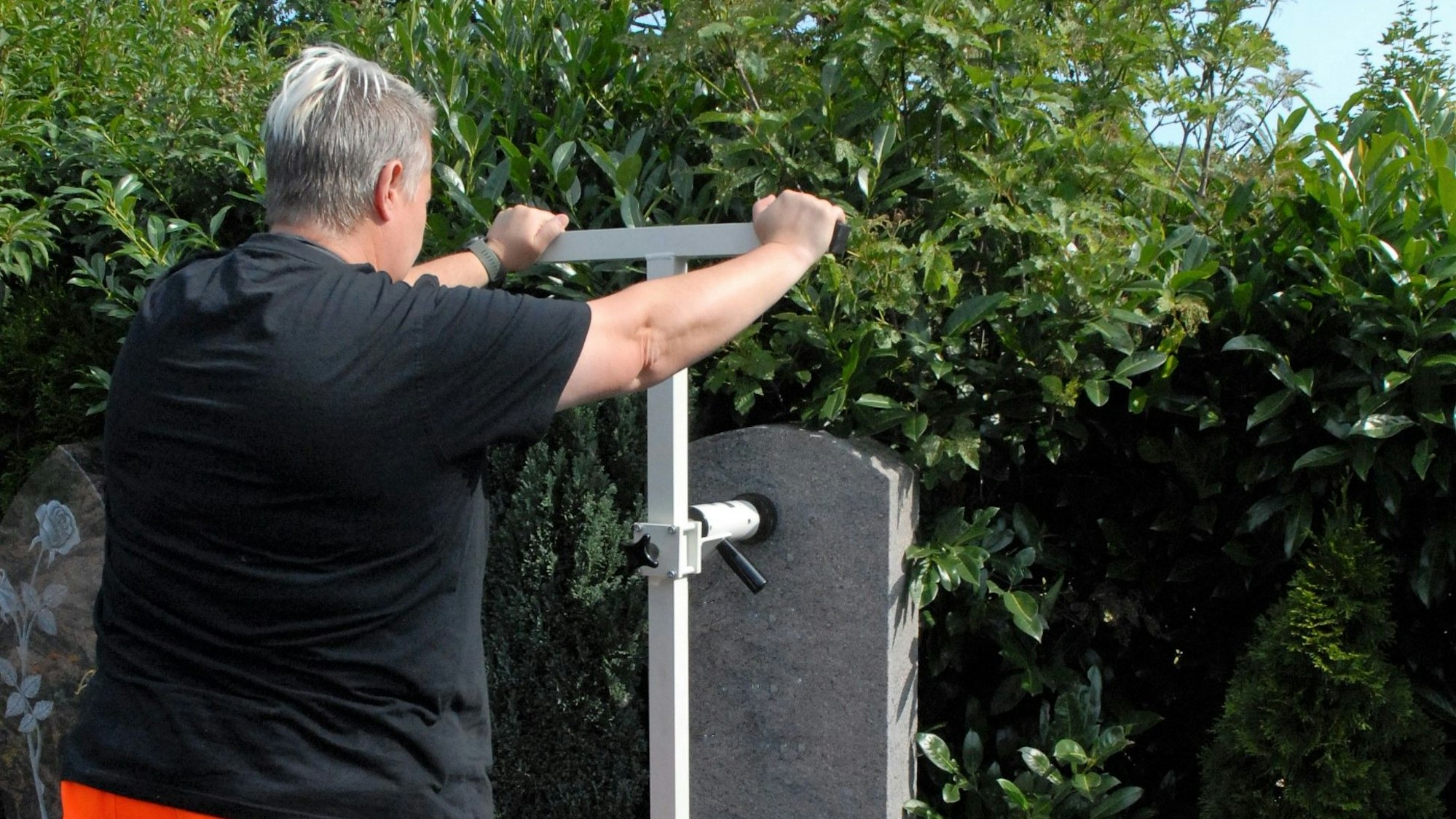 Eine Frau hält ein Messgerät an einen Grabstein.
