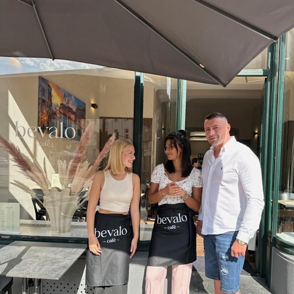 Zwei Frauen und ein Mann stehen vor einem Café.