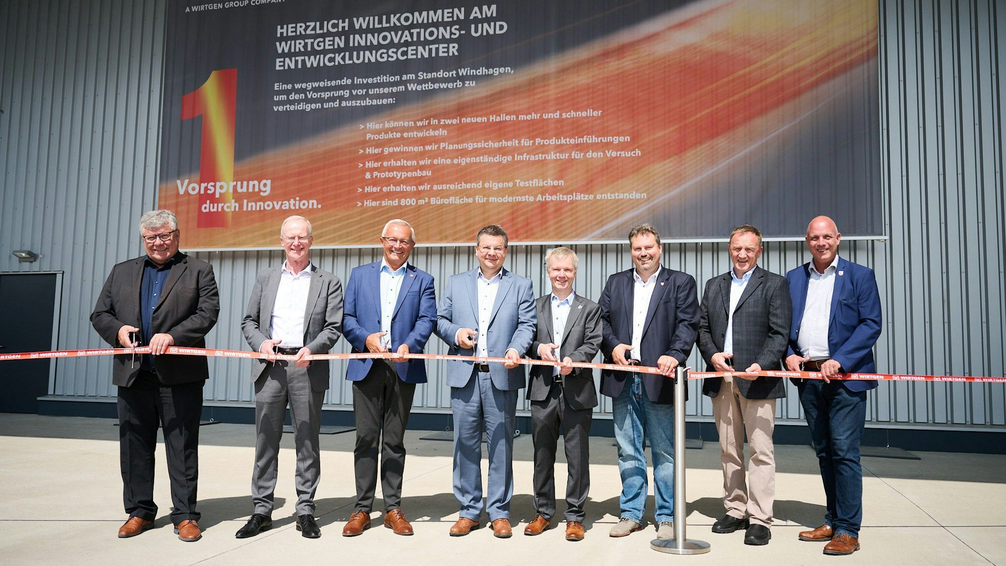 Mehrere Männer schneiden ein symbolisches Band vor dem Zentrum durch.