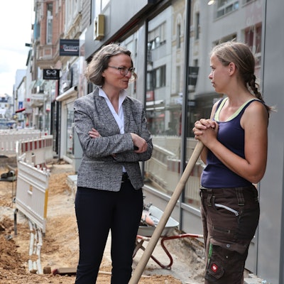 Die Euskirchener Innenstadt ist eine einzige Baustelle. Hier wird neues Pflaster verlegt. An der Baustelle, in der ein Kleinbagger steht, spricht Ina Scharrenbach mit der Praktikantin der Baufirma.