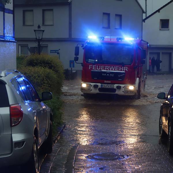 Ein Feuerwehrauto fährt mit Blaulicht in der Dämmerung über eine überflutete Straße.