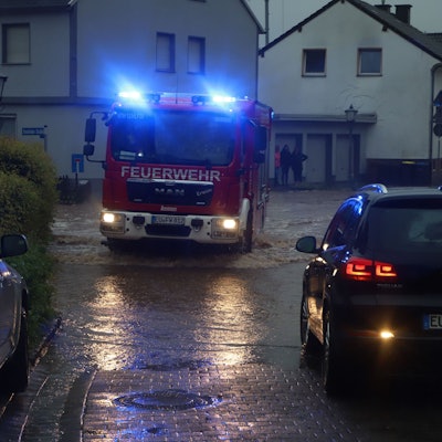 Ein Feuerwehrauto fährt mit Blaulicht in der Dämmerung über eine überflutete Straße.
