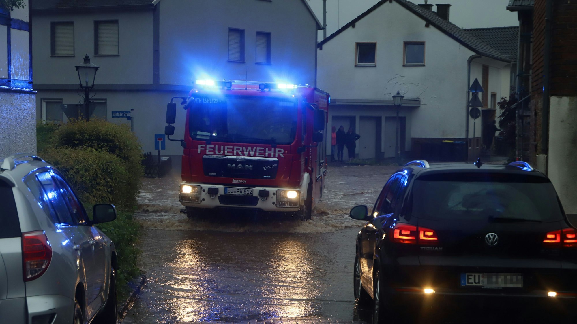 Ein Feuerwehrauto fährt mit Blaulicht in der Dämmerung über eine überflutete Straße.