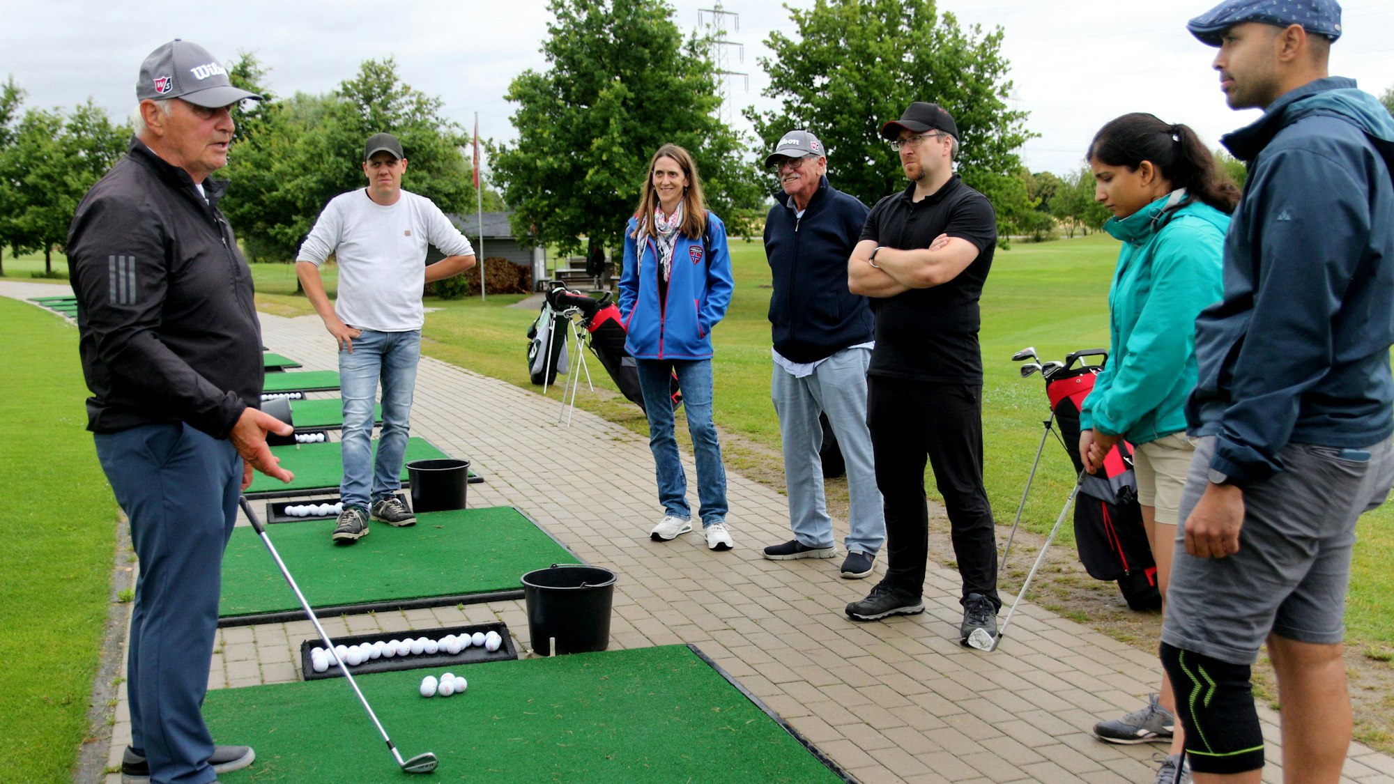 Sechs Golfschüler umringen ihren Trainer, der sie in die Geheimnisse der Golfschläger einweiht.