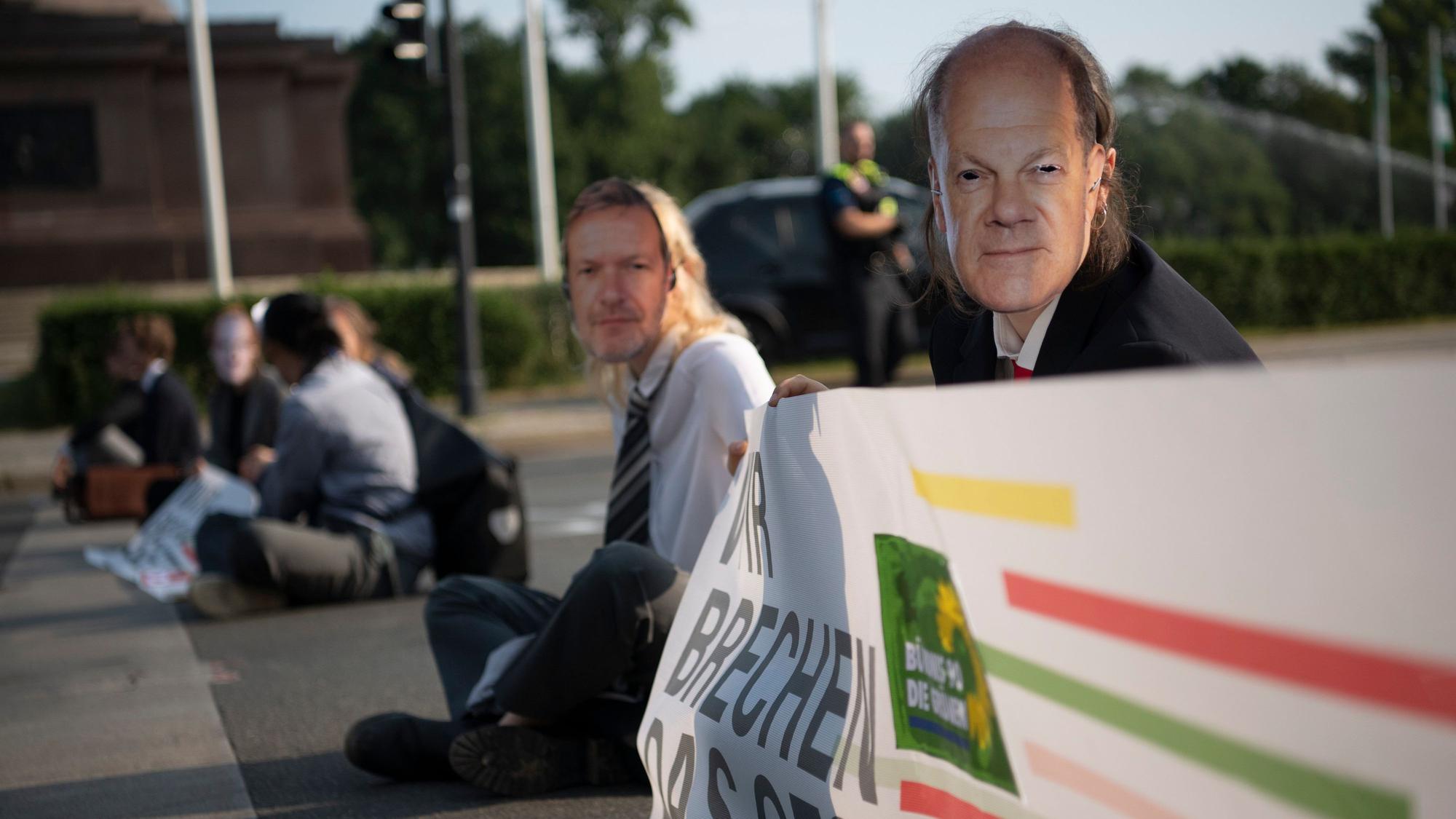 Aktivisten der Gruppe Letzte Generation blockieren am 14. Juli die Fahrbahnen rund um die Siegessäule. Einige von ihnen tragen Masken mit Gesichtern von Ampel-Politikern.