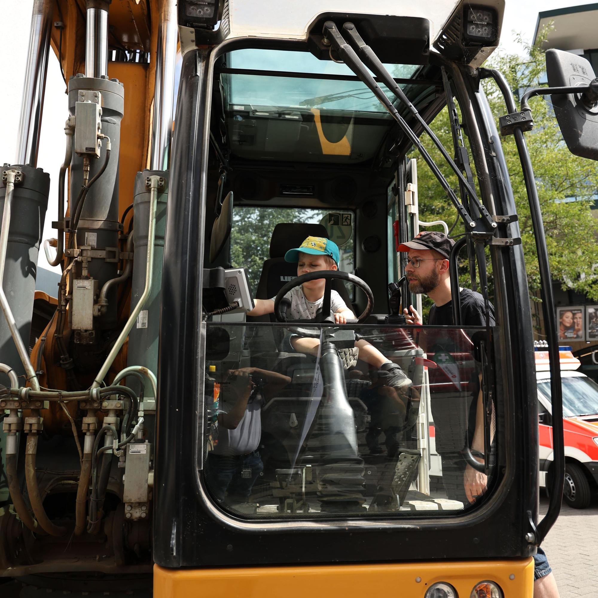 Der kleine Theo sitzt am Steuer des Baggers, steht in der Tür der Kabine und hat ein waches Auge auf ihn.