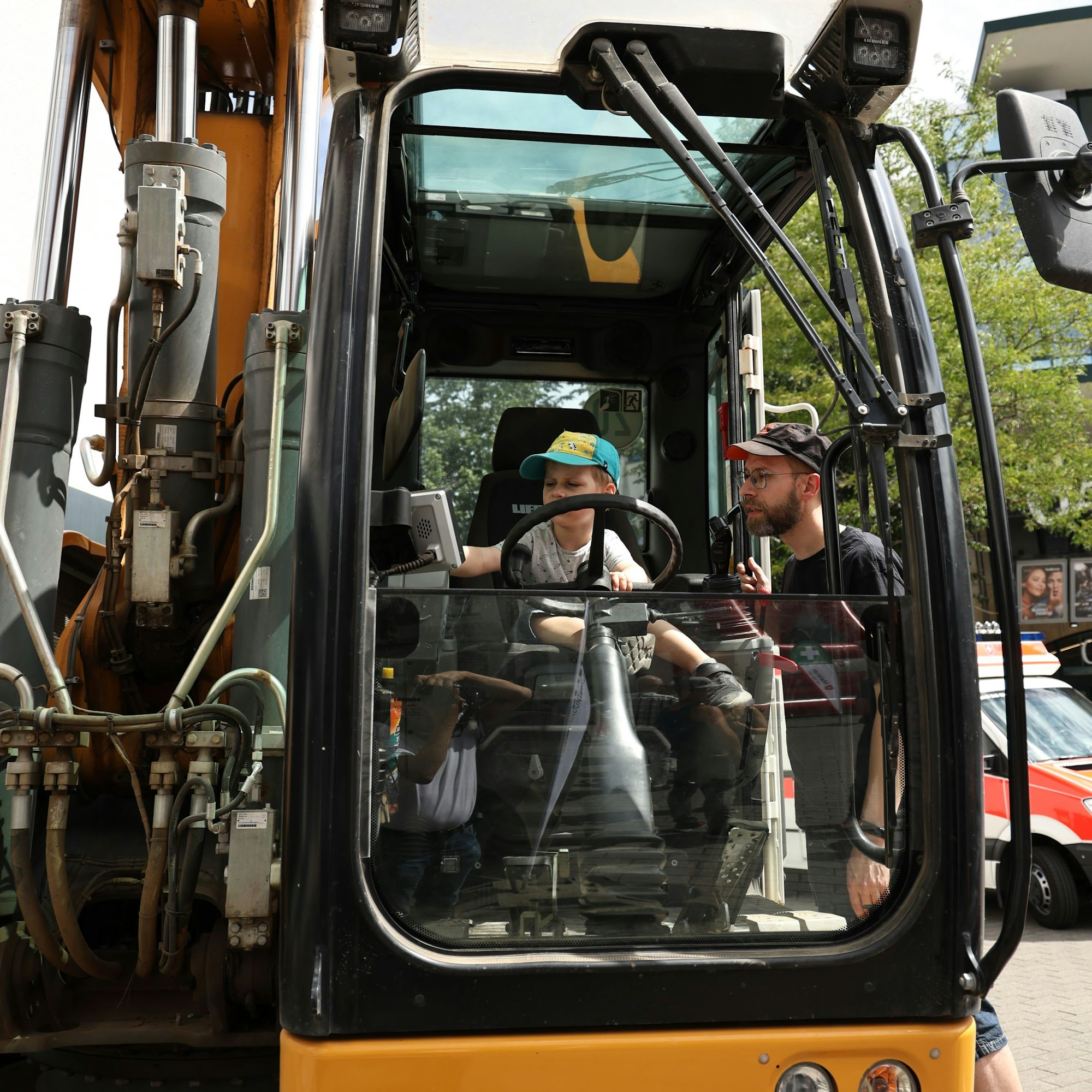 Der kleine Theo sitzt am Steuer des Baggers, steht in der Tür der Kabine und hat ein waches Auge auf ihn.
