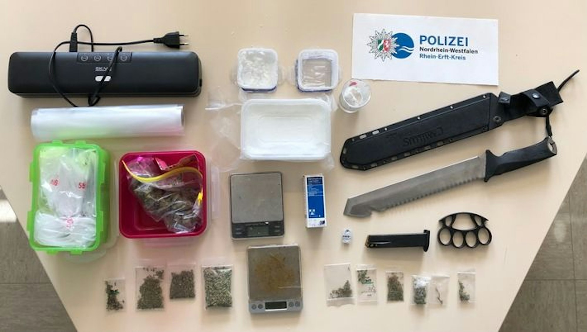 Die beschlangnahmten Gegenstände der Polizei sind auf einem Tisch ausgebreitet, darunter eine Machete, Marihuana und Amphetamine.
