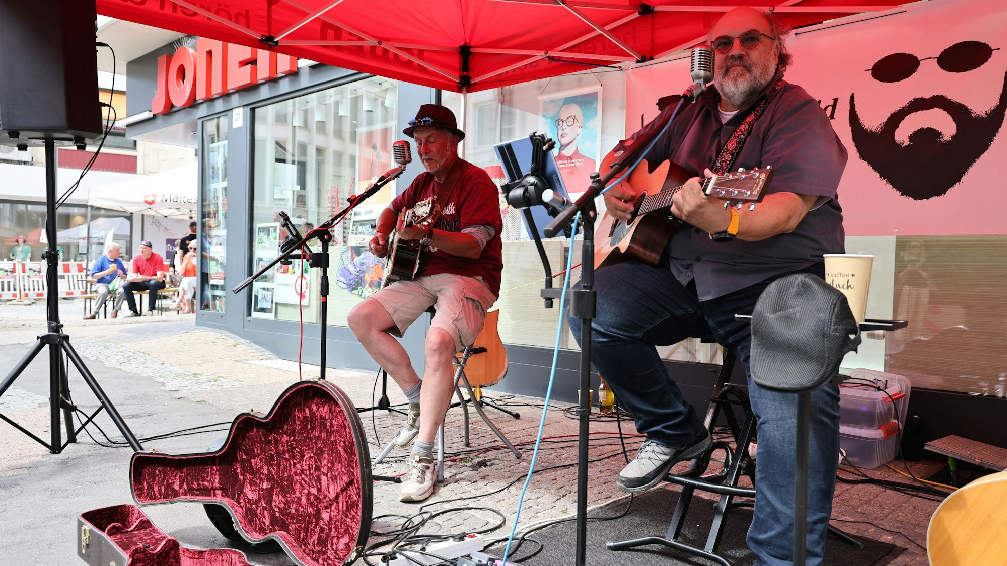 Die beiden Musiker mit ihren Gitarren, vor ihnen ein Gitarrenkoffer mit Münzen drin.