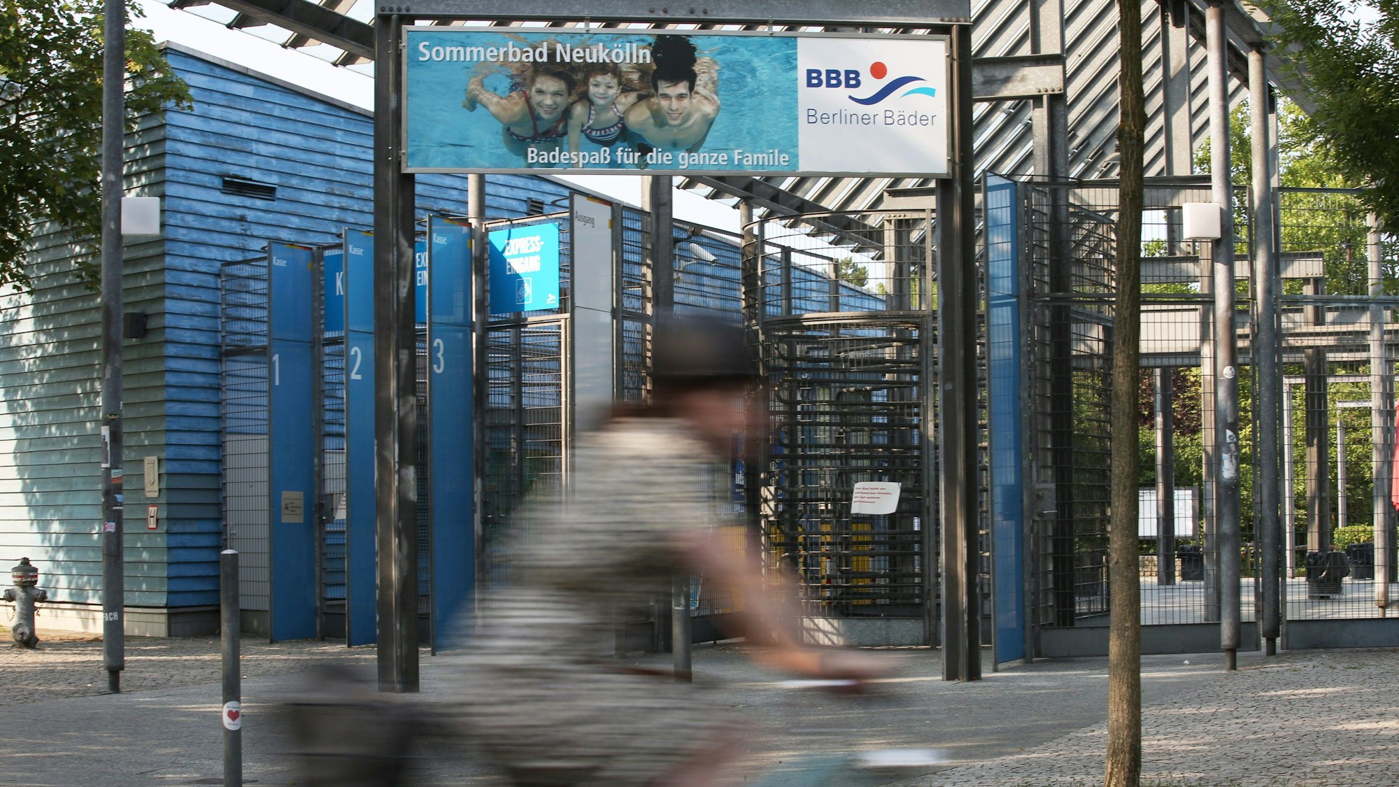 14.07.2023, Berlin: Eine Fahrradfahrerin fährt nahe des geschlossenen Eingangs des Columbiabads in Neukölln vorbei, an dem ein Hinweisschild mit der Aufschrift „Das Bad bleibt aus betrieblichen Gründen bis auf weiteres geschlossen!“ hängt.
