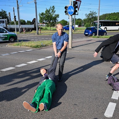 Ein Mitglied der Protestgruppe Letzte Generation wird bei einer Sitzblockade an der Autobahnabfahrt am Elbepark von einem Autofahrer (M) beiseite gezogen. Die Demonstranten tragen Masken mit den Portraits von Bundeswirtschaftsminister Habeck (l) und Bundeskanzler Scholz.