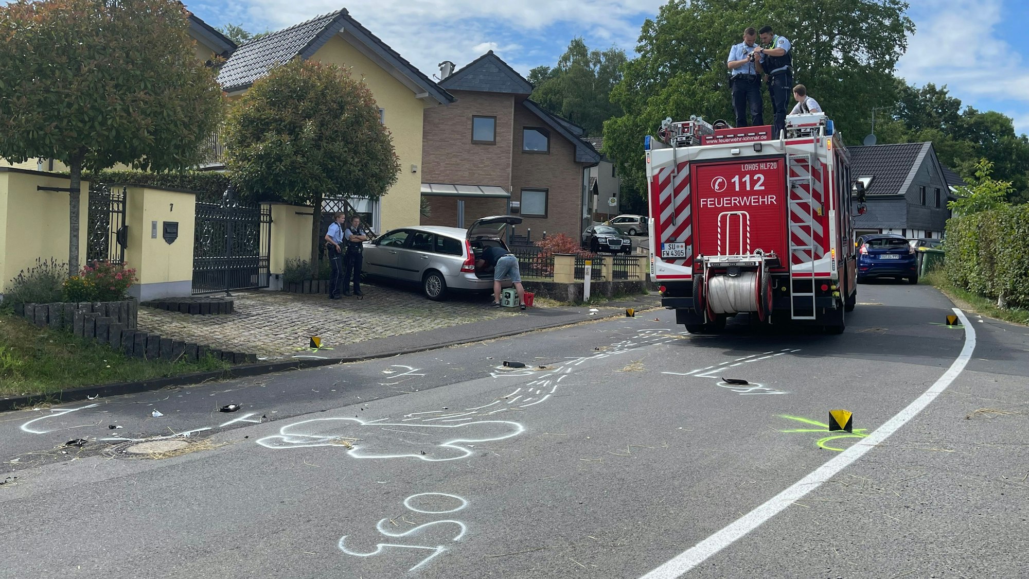 Trümmerteile liegen nach dem Unfall auf der Fahrbahn verstreut, die Polizei fotografiert die Spuren vom Dach eines Löschfahrzeugs, Markierungen wurden auf die Fahrbahn gesprüht.
