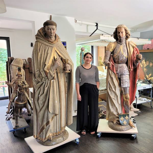 Eine Frau steht zwischen zwei großen Heiligenfiguren in einem Atelier.