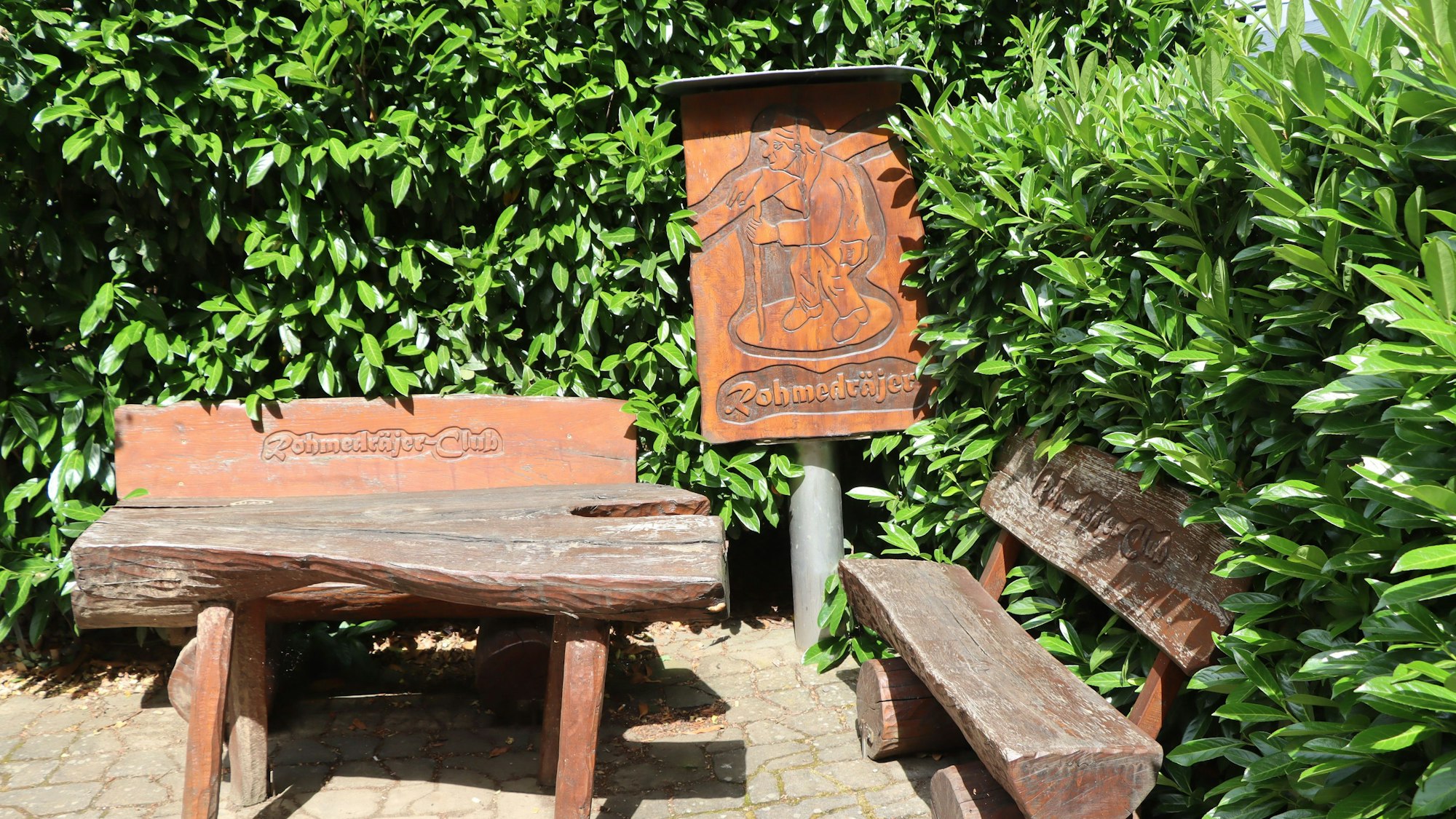 Zwischen grünen Hecken stehen ein Tisch und zwei Bänke.