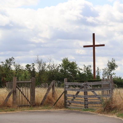 Hinter einem Weidezaun steht ein großes Holzkreuz.