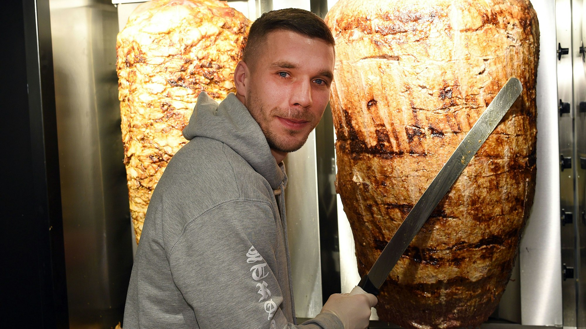 FC-Ikone Lukas Podolski steht bei der Eröffnung eines Döner-Ladens in Köln an einem Fleischspieß. In Lokal der Kette „Mangal Döner“ wurde kurz vor der Eröffnung in Mönchengladbach mit Farbe beschmiert. (Archivbild)