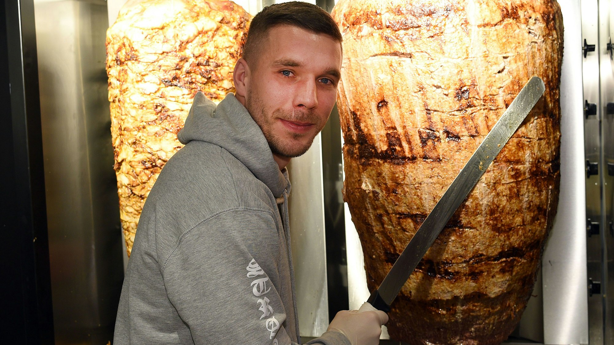 Fußball-Weltmeister Lukas Podolski steht bei der Eröffnung eines Döner-Ladens an einem Dönerspieß.