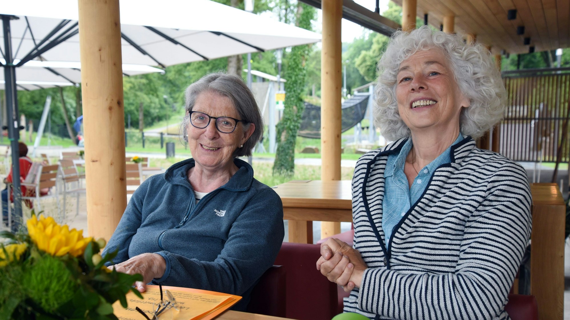Unter dem schützenden Dach des neuen Seecafés, aber draußen haben Susanne Focke-Gebauer aus Wiehl (l.) und Berna Kühn aus Bergisch Gladbach Platz genommen. Sie genießen die ersten Getränke ebenso wie den Ausblick dort.