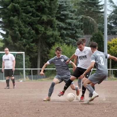 Kalls David vom Berg wird von zwei Vernicher Spielern in grauen Trikots angegriffen. Die Asche auf dem Platz in Keldenich staubt.