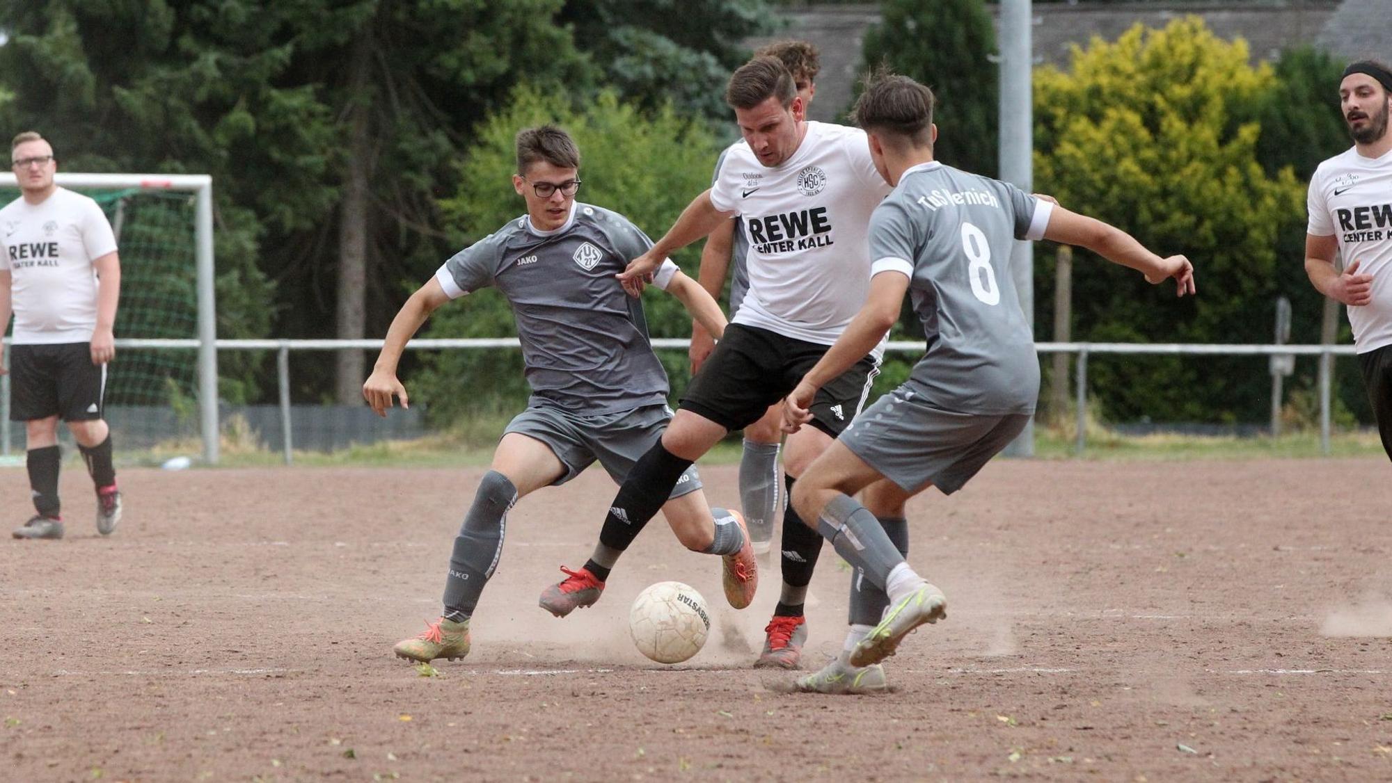 Kalls David vom Berg wird von zwei Vernicher Spielern in grauen Trikots angegriffen. Die Asche auf dem Platz in Keldenich staubt.