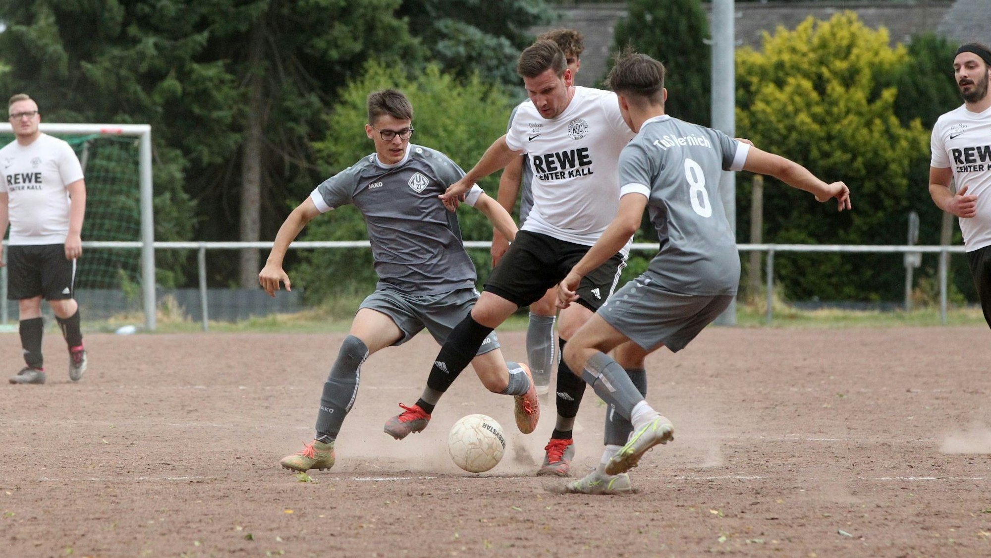 Kalls David vom Berg wird von zwei Vernicher Spielern in grauen Trikots angegriffen. Die Asche auf dem Platz in Keldenich staubt.